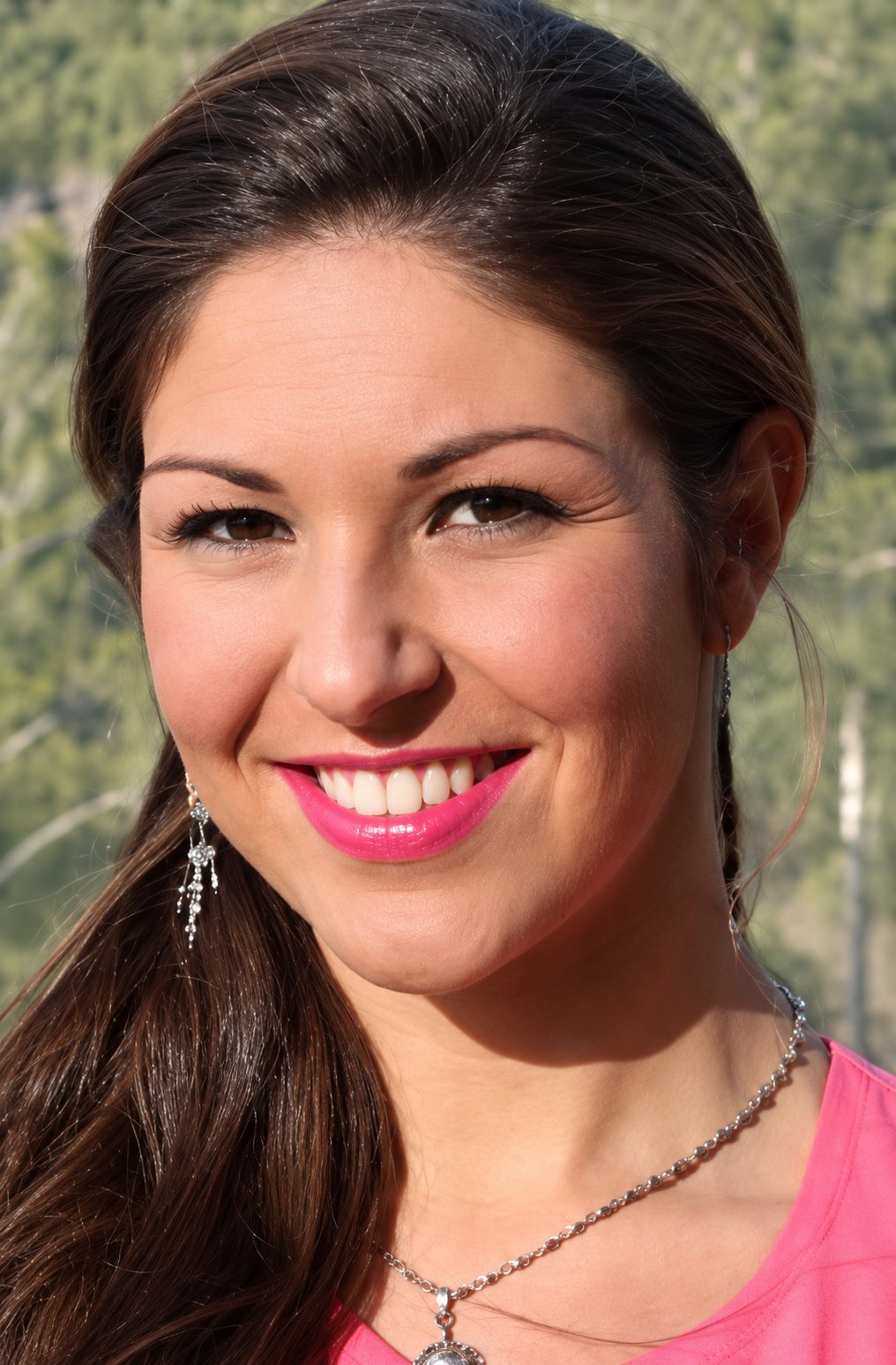 Portrait de Marylaure, souriante, rouge à lèvres rose, boucles d'oreilles pendantes et collier, devant un fond de verdure